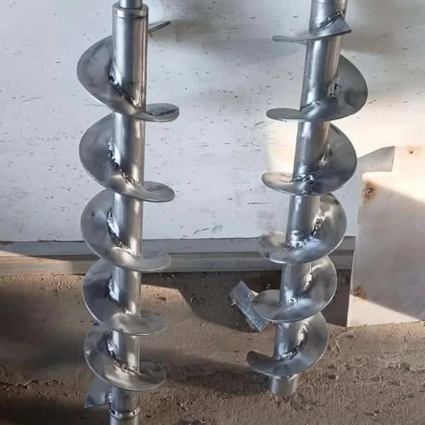 Two metal shafts with helical screw flights standing on a workshop bench.