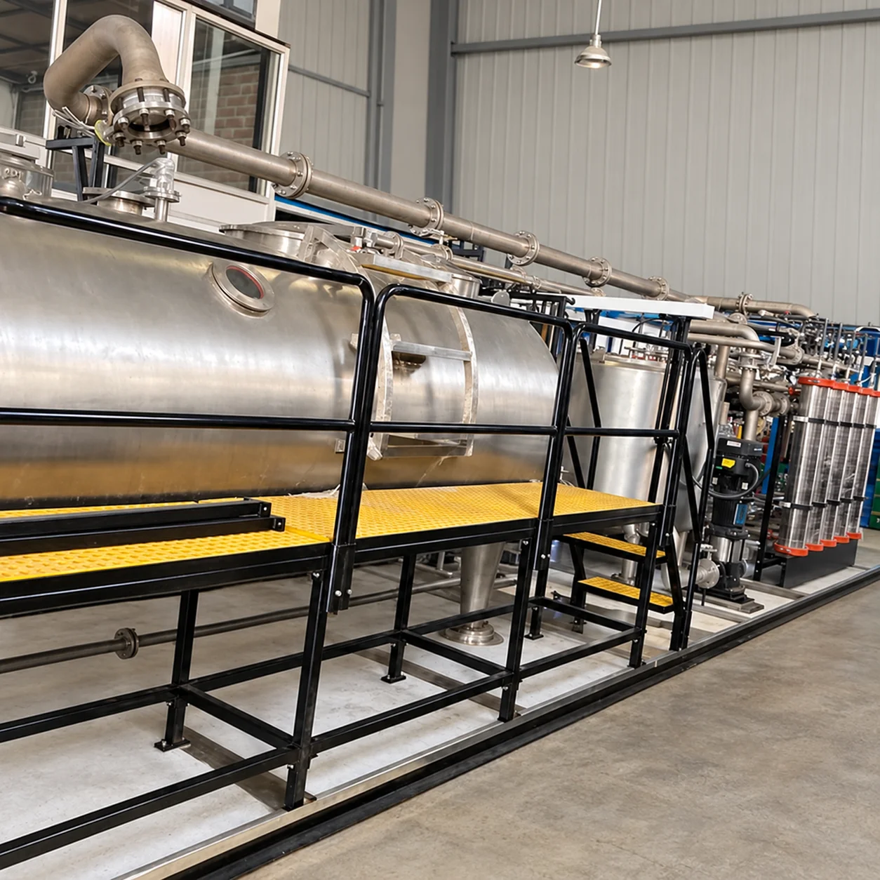 Paint filter machine with a stainless steel vessel, pipework, black frame, yellow walkway, and filter assembly.